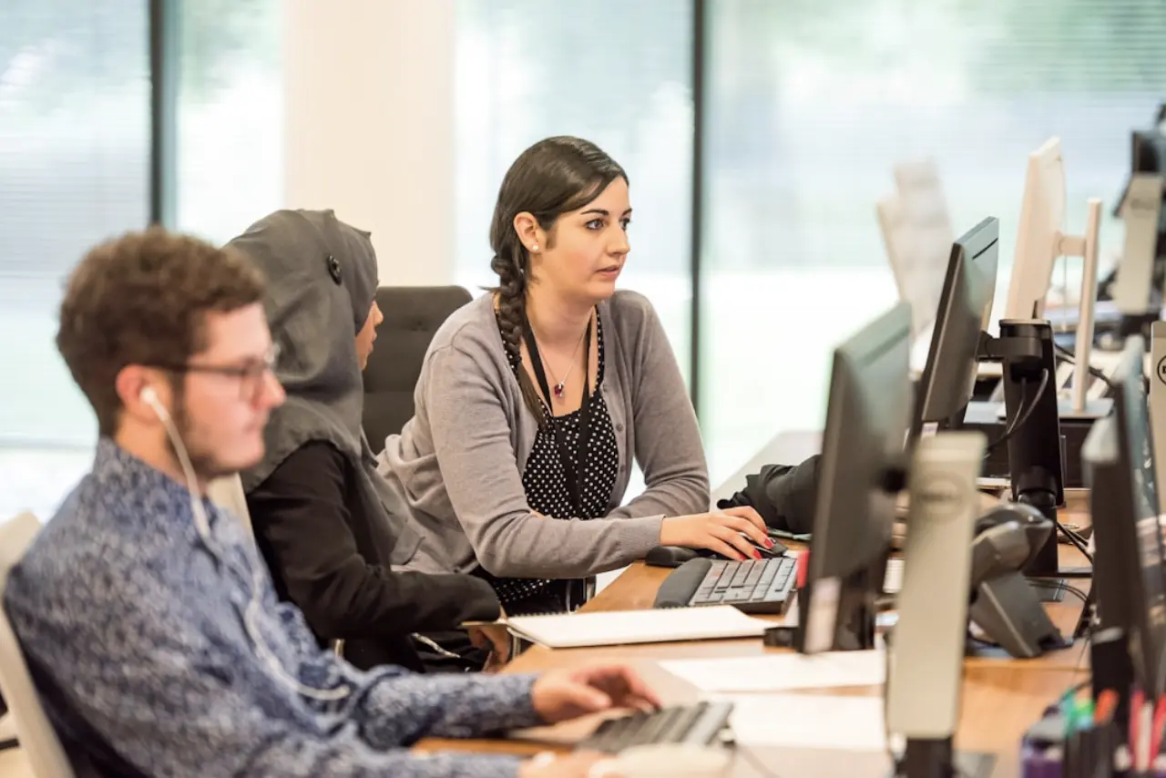 Individuals focused on their computers, engaged in teamwork within a contemporary office setting.

